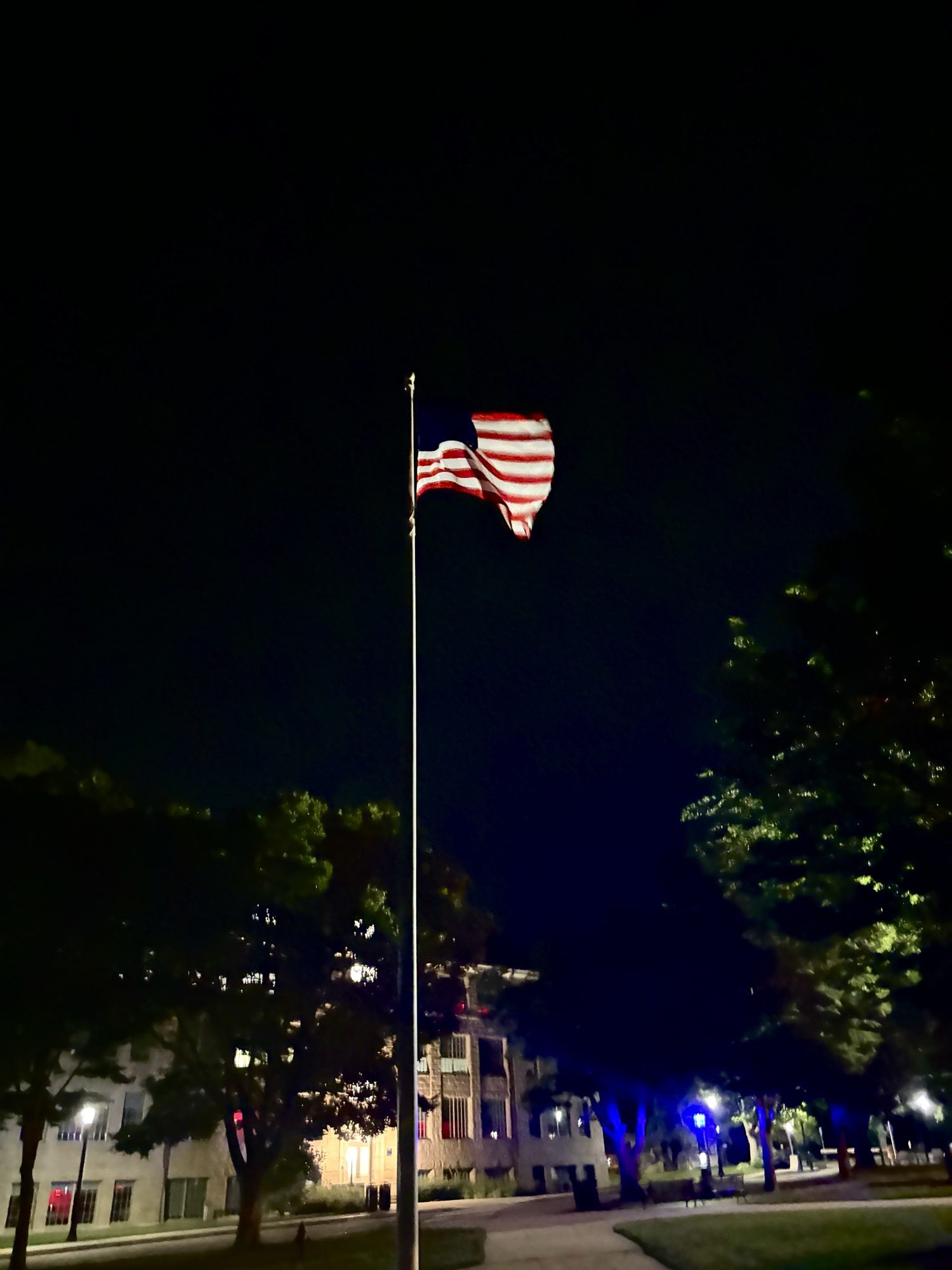American flag lit against the night sky above campus buildings