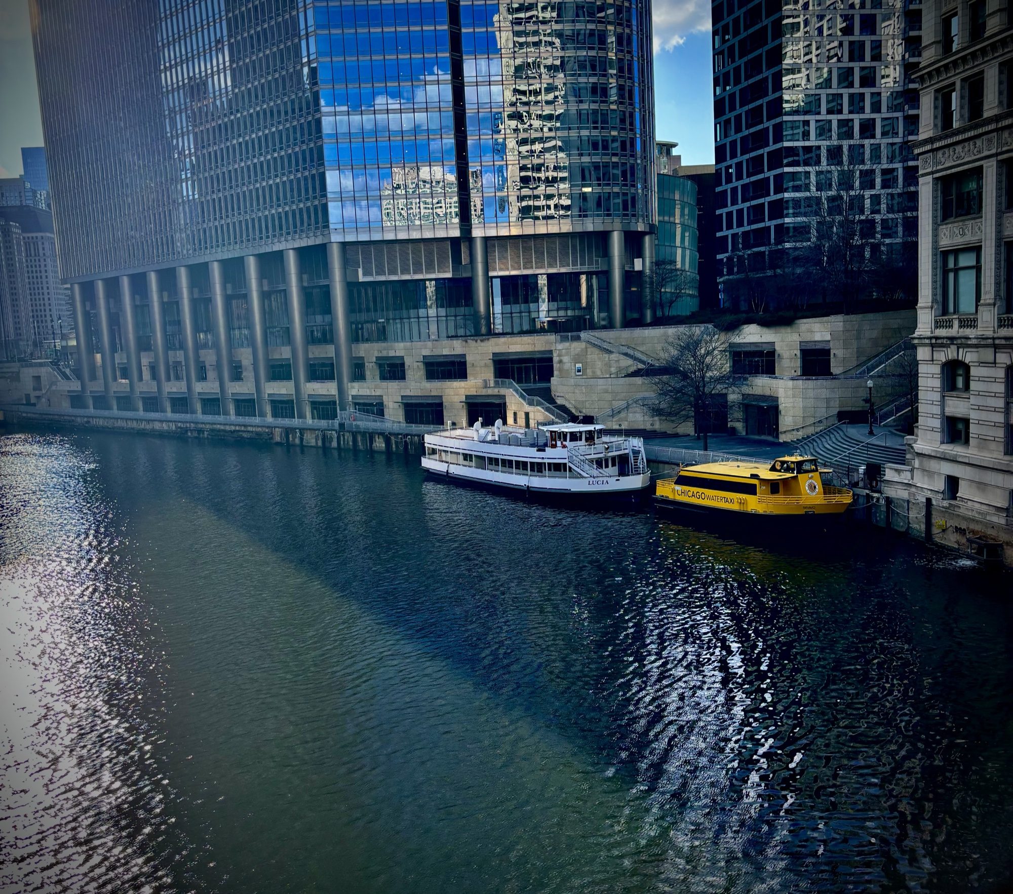 Chicago River lined with glass towers, with tour boats docked along the bank