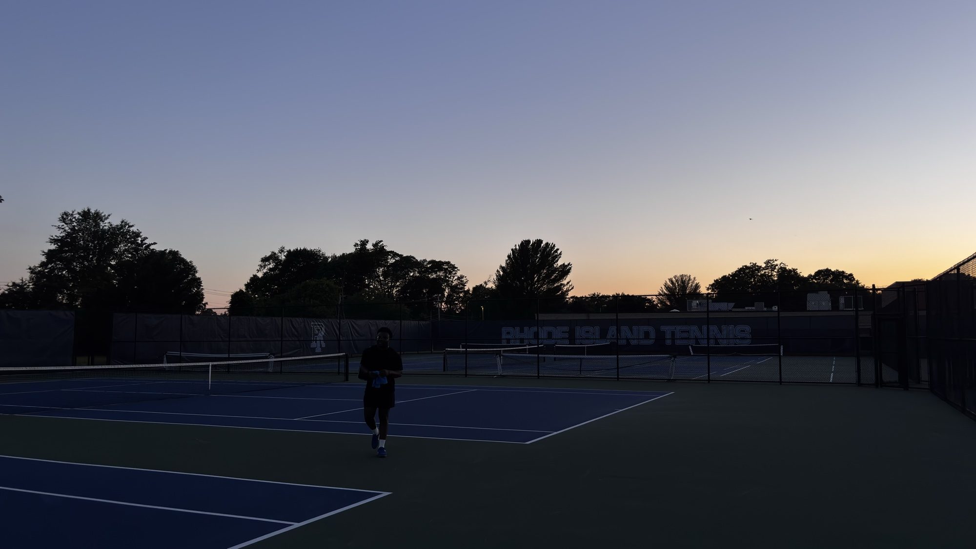 Tennis courts at dusk with a player on the far court