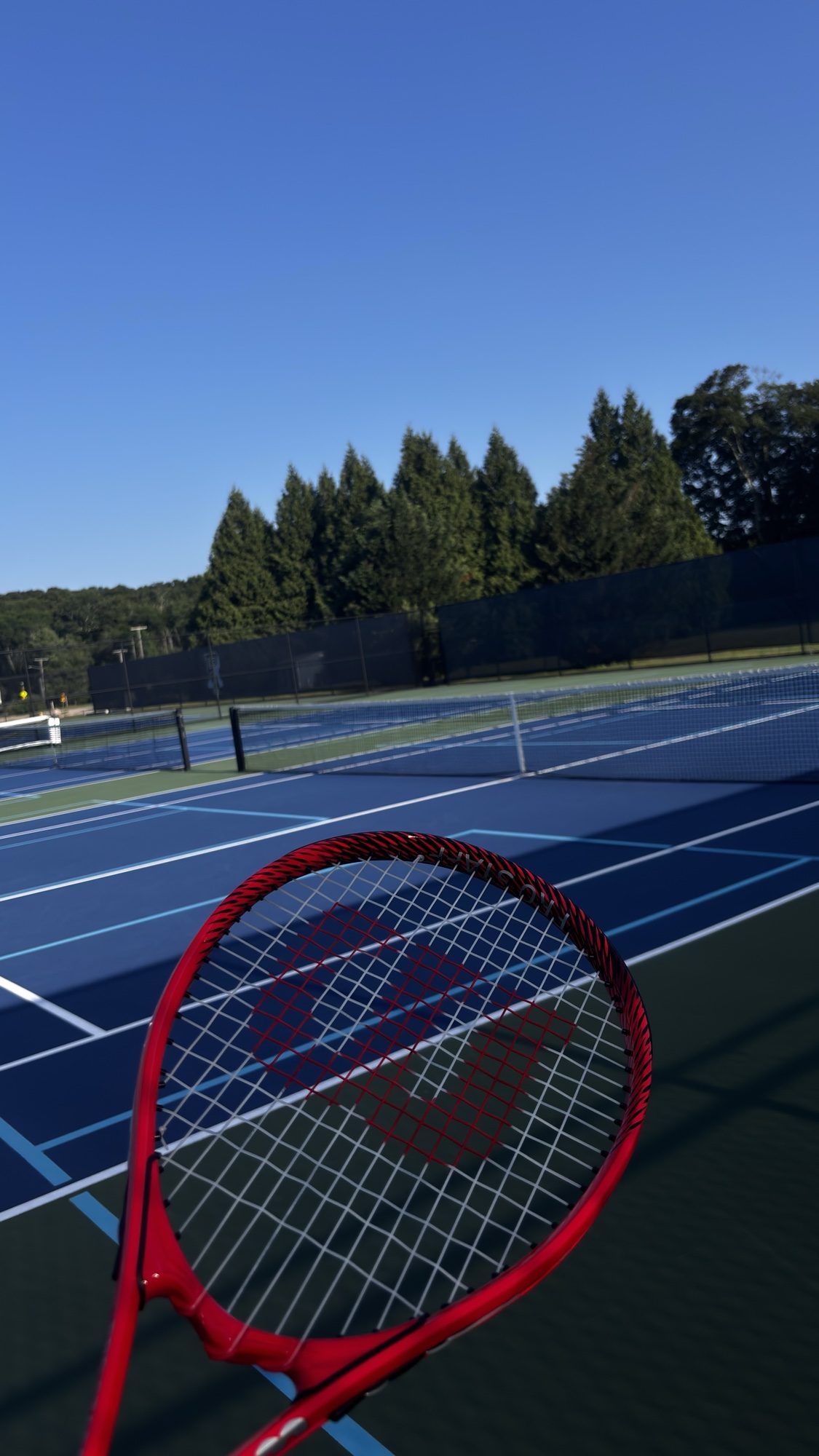 Red tennis racket held over a blue tennis court