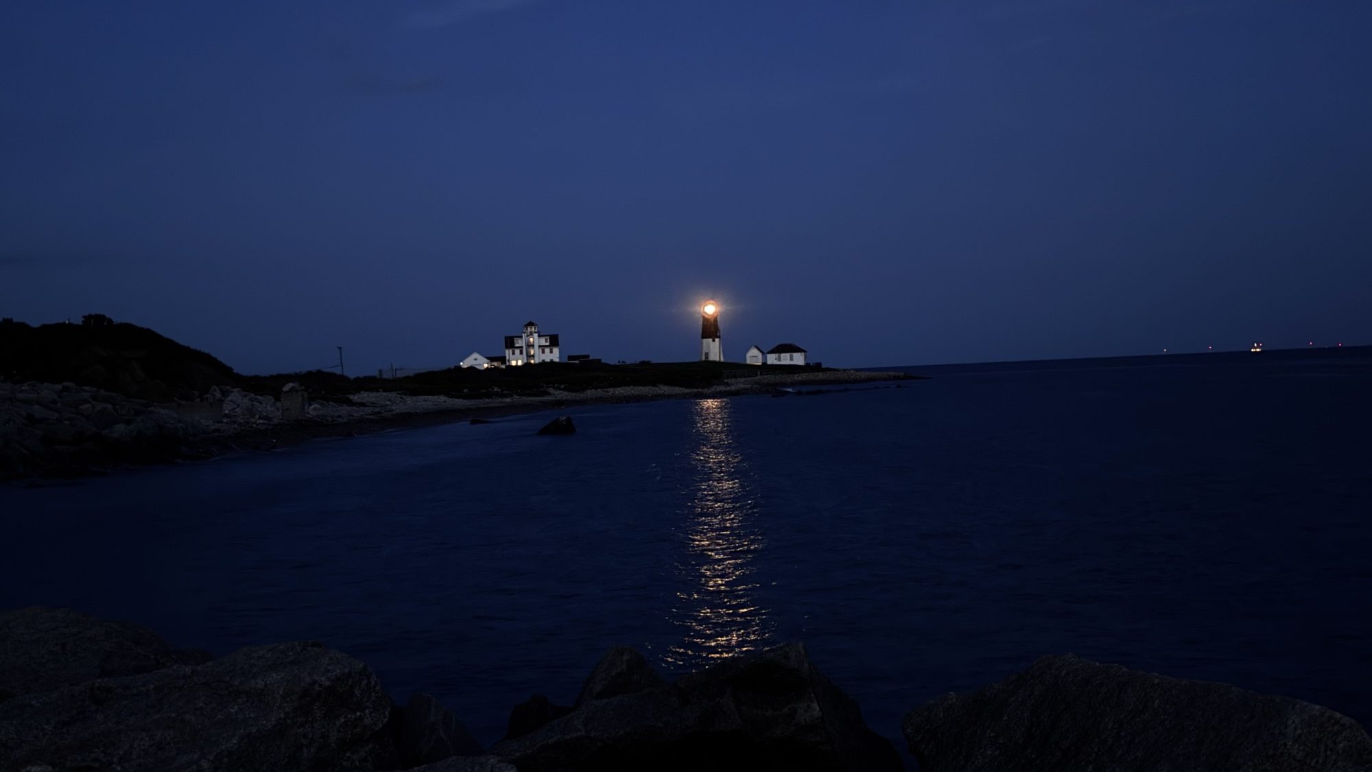 Lighthouse on a rocky point at night, its light reflecting on the water