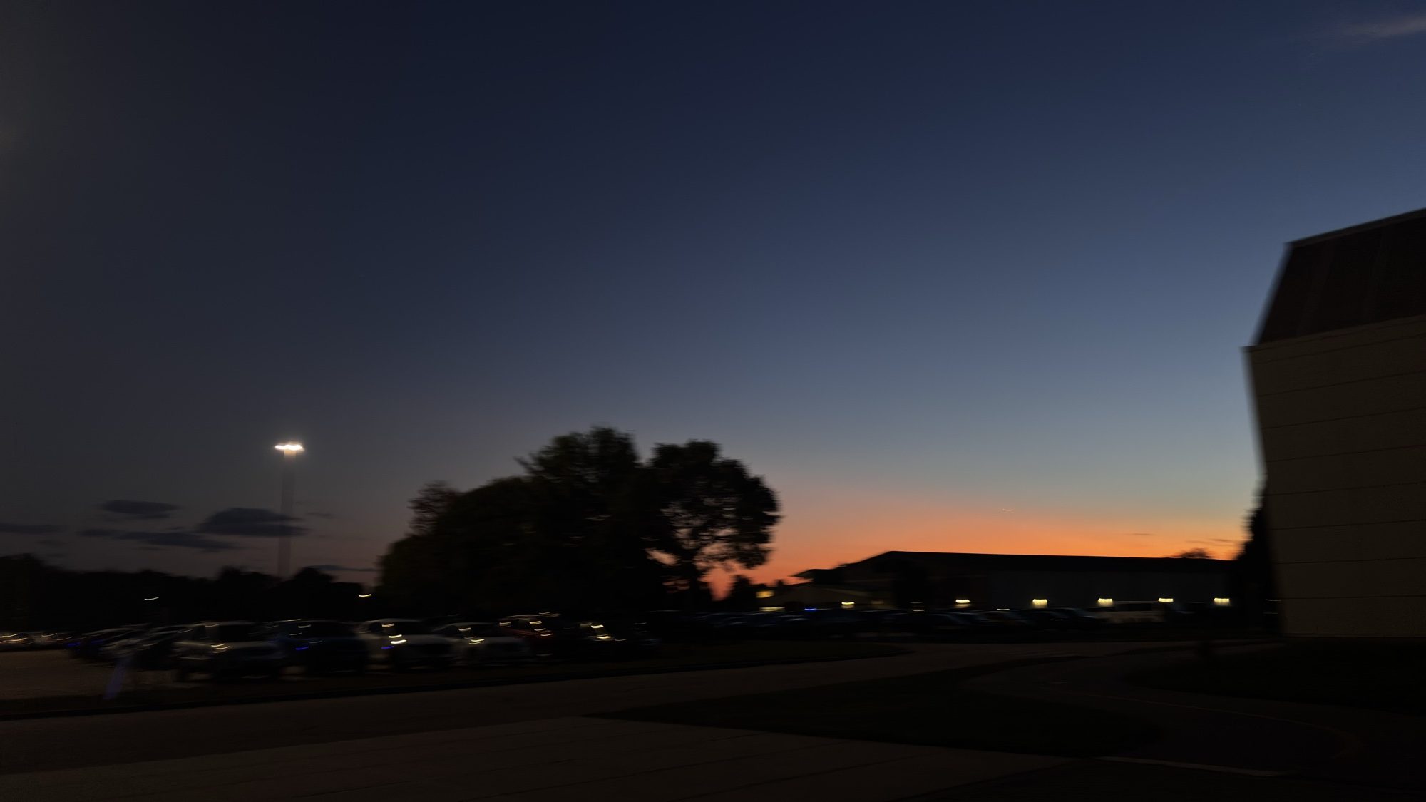 Dusk sky glowing orange behind trees and the silhouette of a building